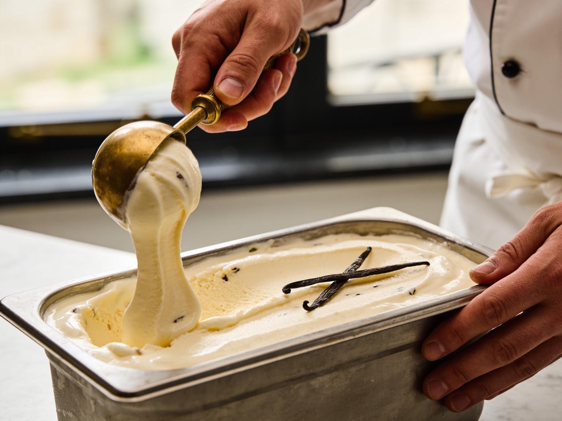 A gold scoop drawn through fresh vanilla ice cream, split vanilla pods alongside
